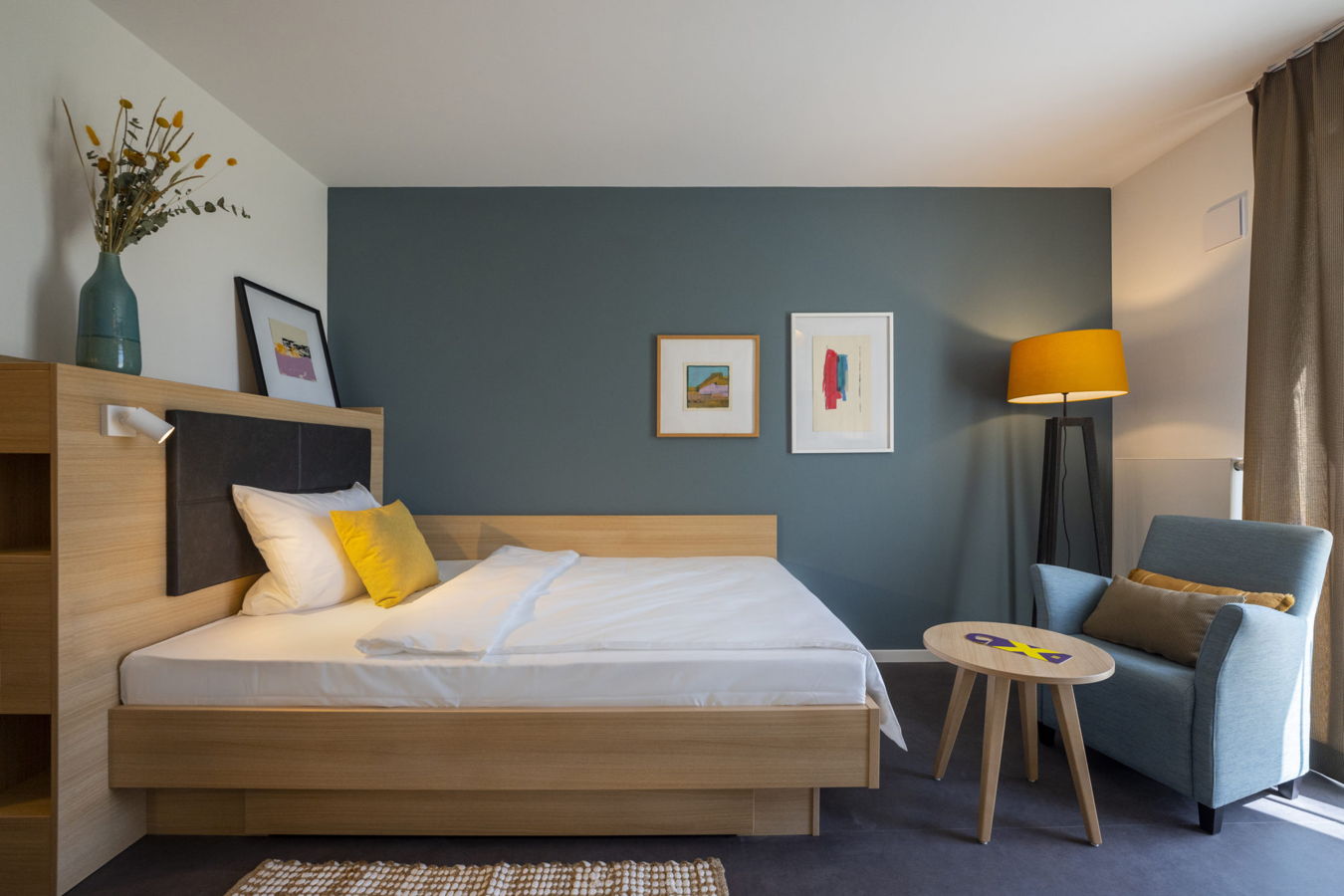 Modern eingerichtetes Hotelzimmer mit Bett, Sessel, Lampe und kleinem Tisch