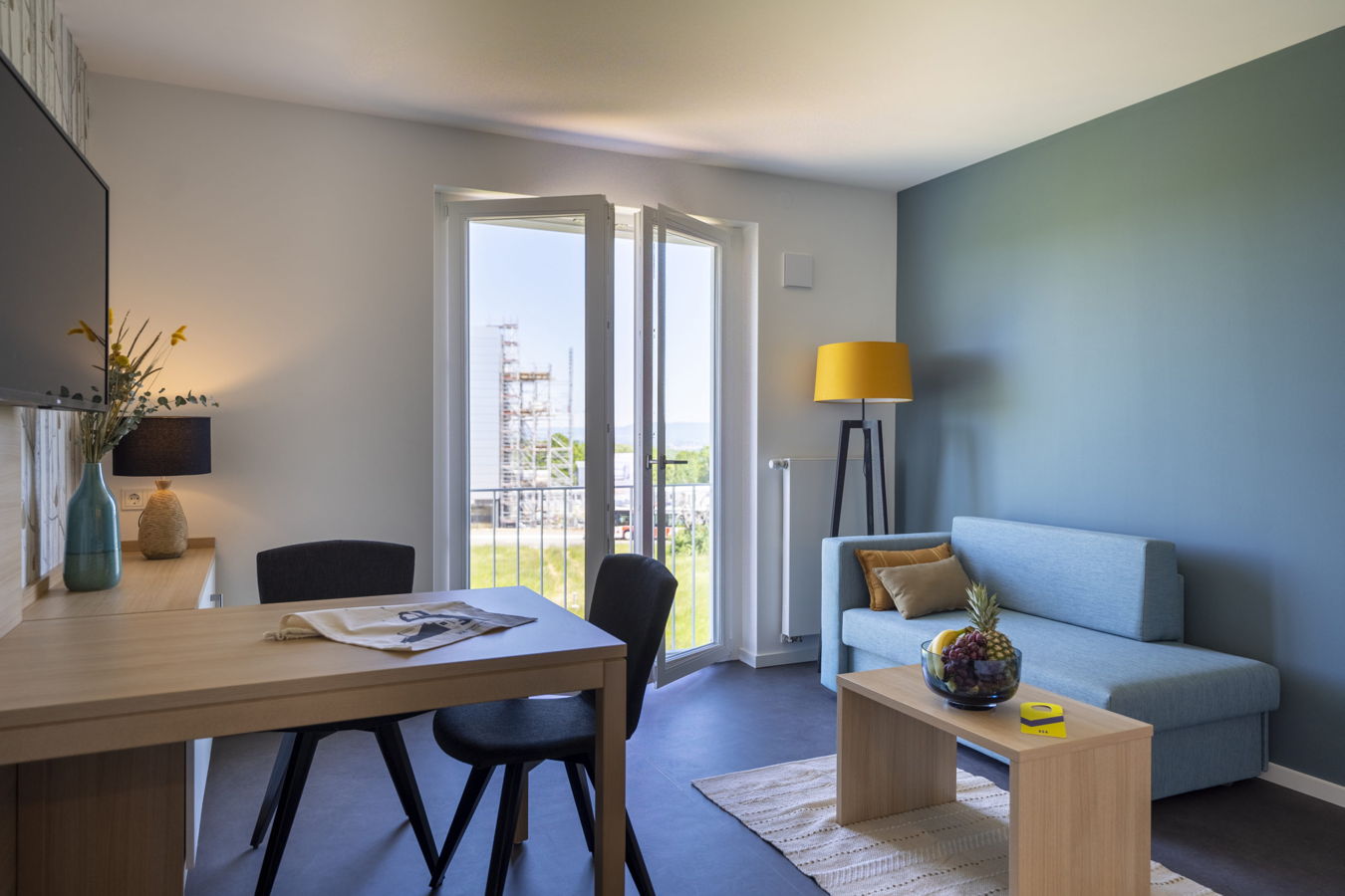Modern eingerichtetes Wohnzimmer mit Esstisch, Sofa, Stehlampe und offenem Balkontürzugang