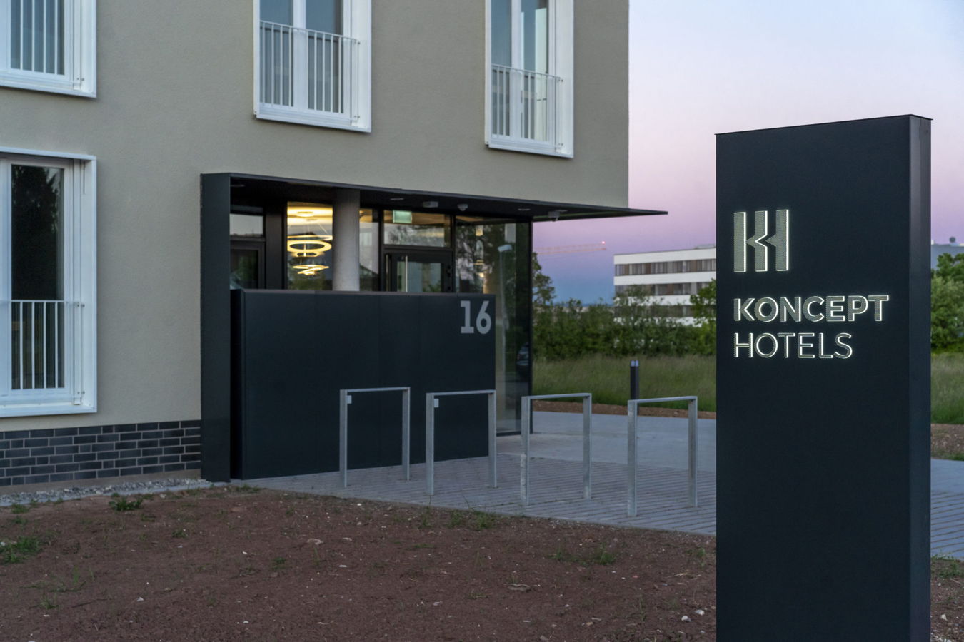 Eingang eines Koncept Hotels mit beleuchtetem Schild und der Hausnummer 16
