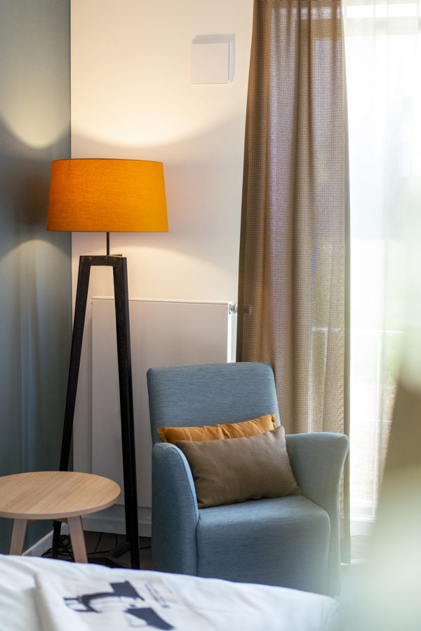 Gemütliche Sitzecke mit blauem Sessel, Stehlampe und Vorhang am Fenster