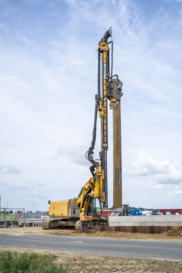 Bagger mit Rammgerät beim Einrammen eines Stahlpfahls auf einer Baustelle