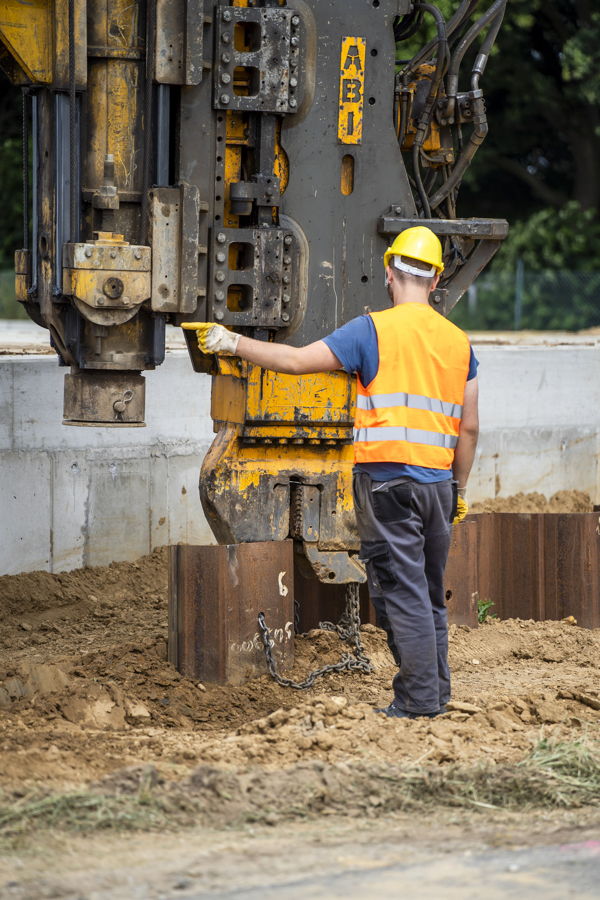 Bauarbeiter in Warnweste und Helm bedient eine schwere Rammmaschine auf einer Baustelle