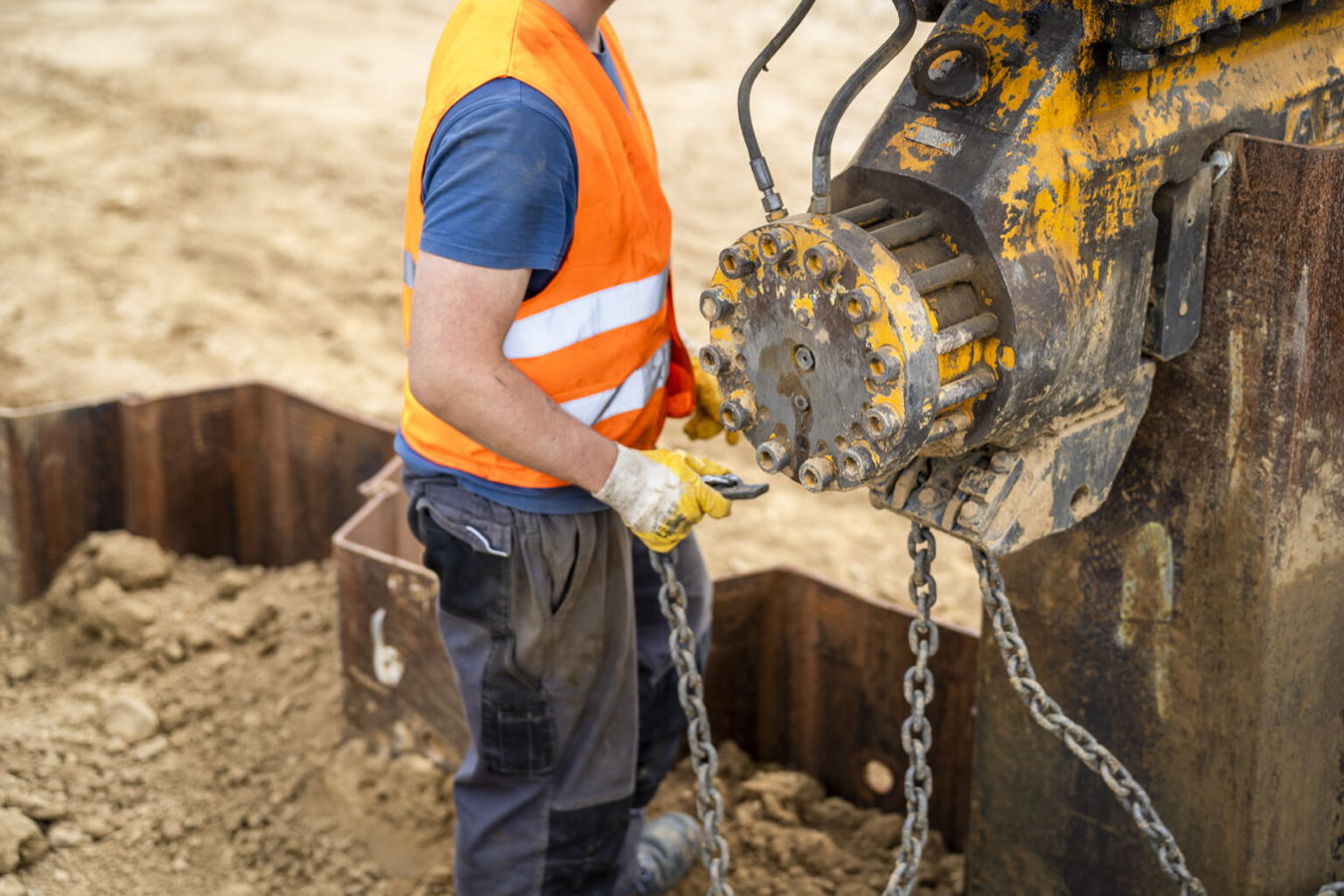 Bauarbeiter in Warnweste bedient einen Baggeranbau auf einer Baustelle
