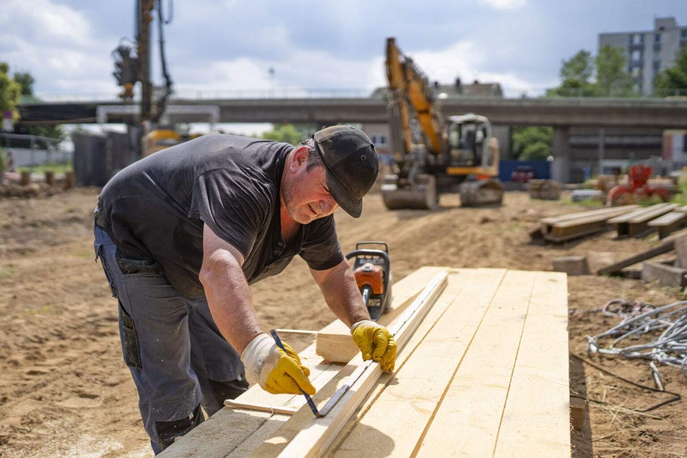 Ein Bauarbeiter misst und markiert Holzbretter auf einer Baustelle