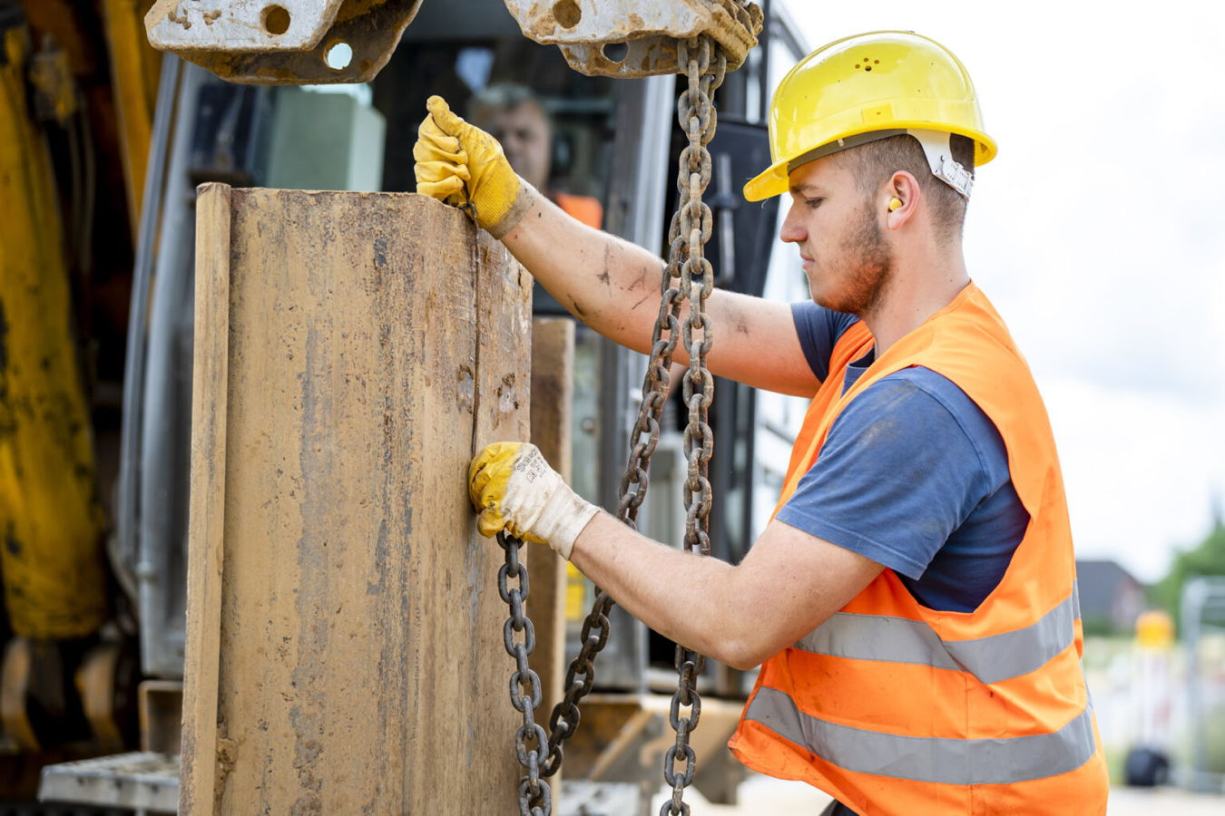 Bauarbeiter befestigt eine schwere Metallplatte mit Ketten an einer Baumaschine