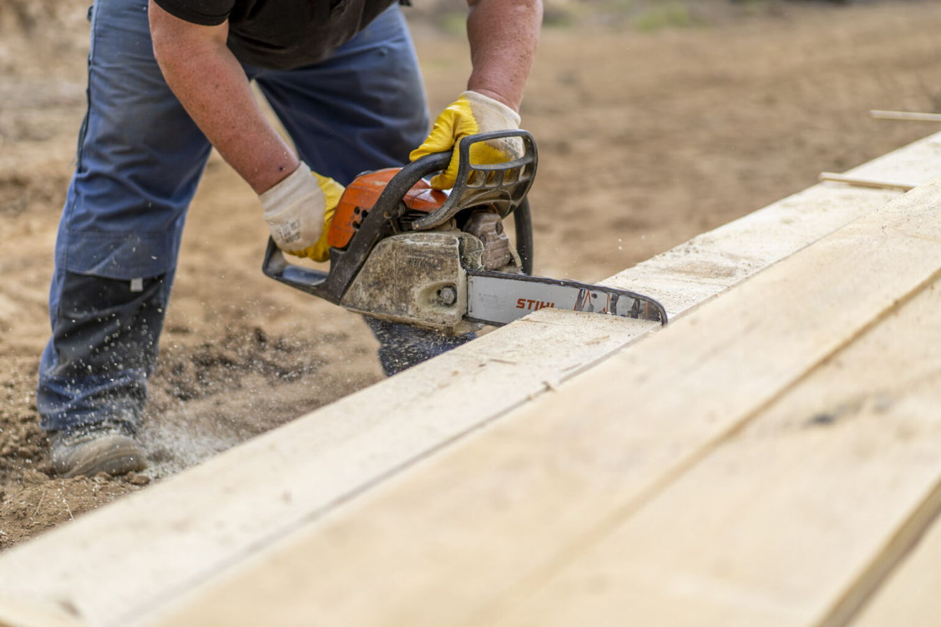 Ein Arbeiter sägt mit einer Kettensäge ein Holzbrett zu