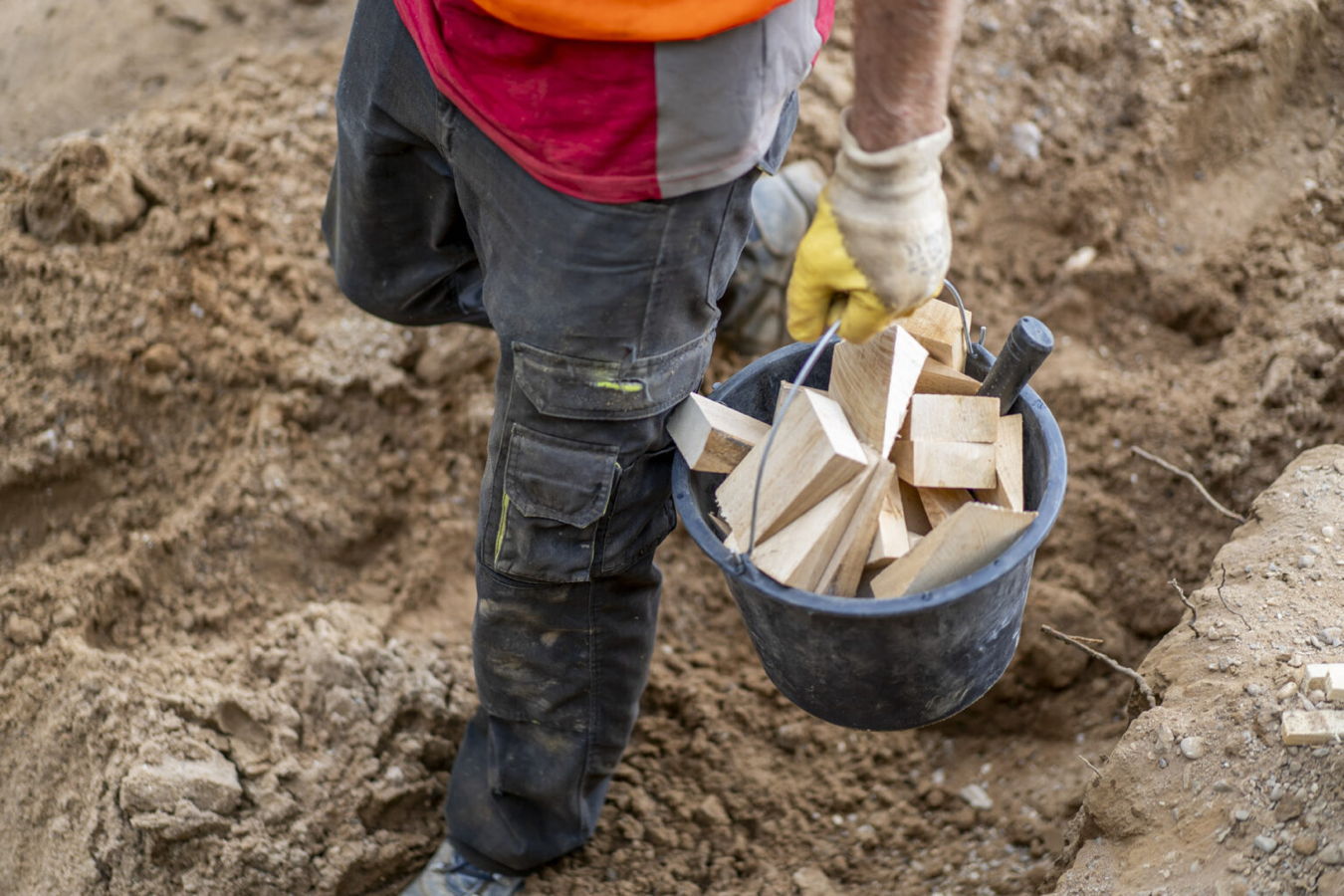 Arbeiter trägt einen Eimer mit Holzkeilen in einer Erdgrube