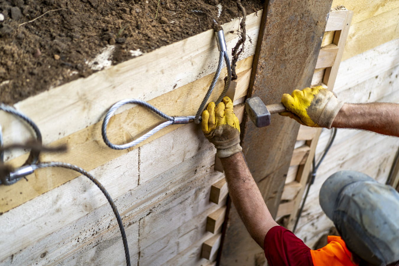 Arbeiter sichern eine Baugrube mit Stahlseilen und Holzbohlen