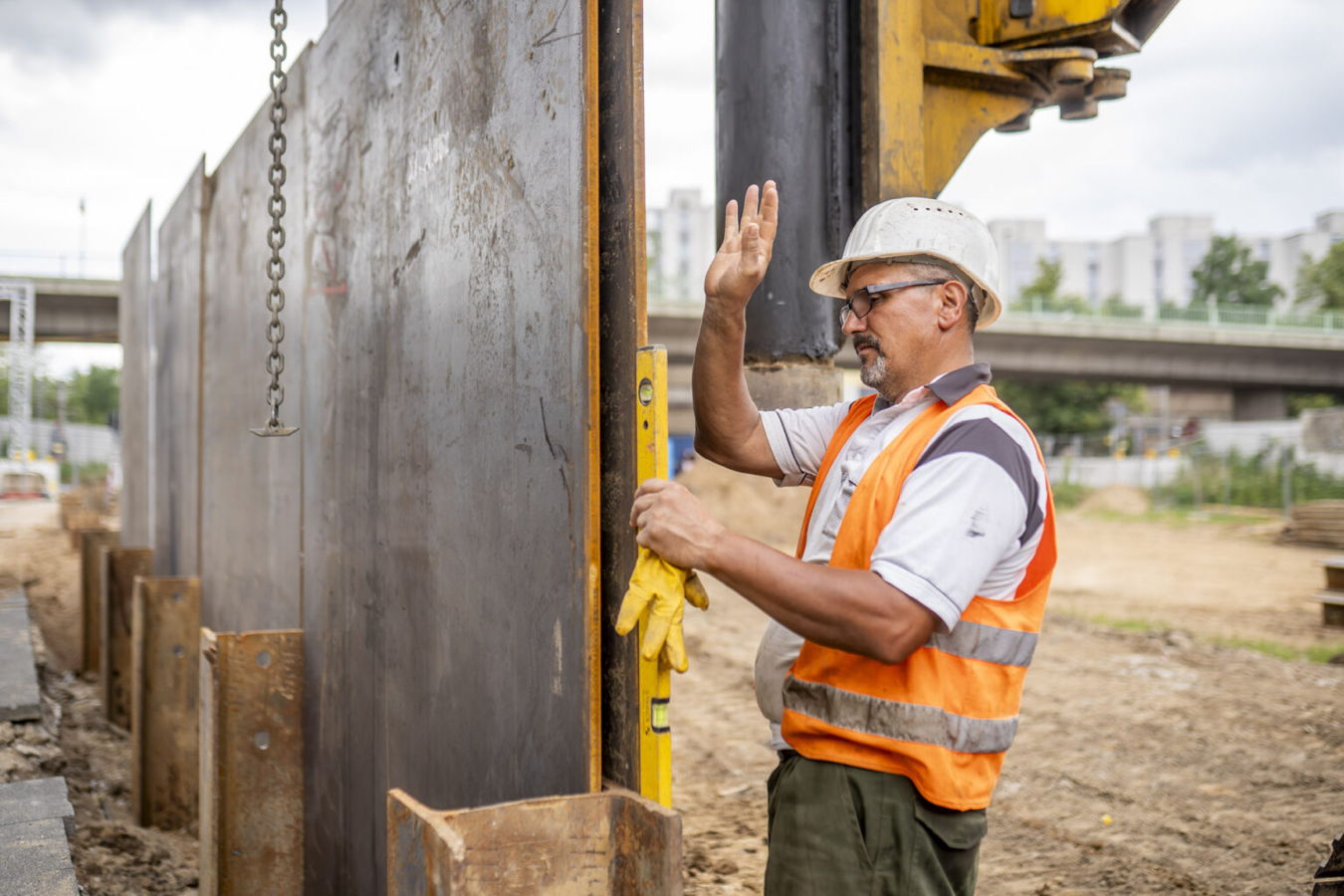 Bauarbeiter mit Helm und Warnweste misst an einer Stahlwand auf der Baustelle
