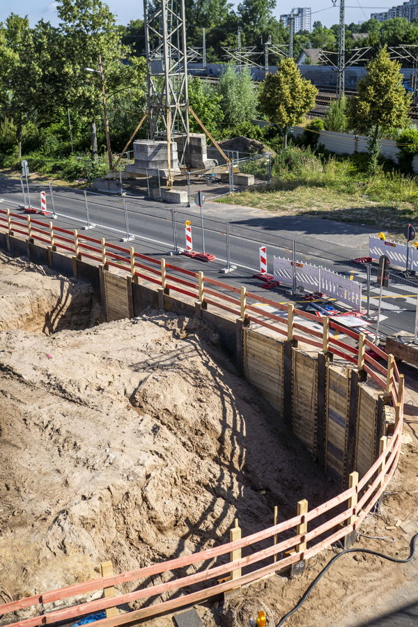 Große Baugrube an einer gesperrten Straße neben Bahngleisen und Strommasten