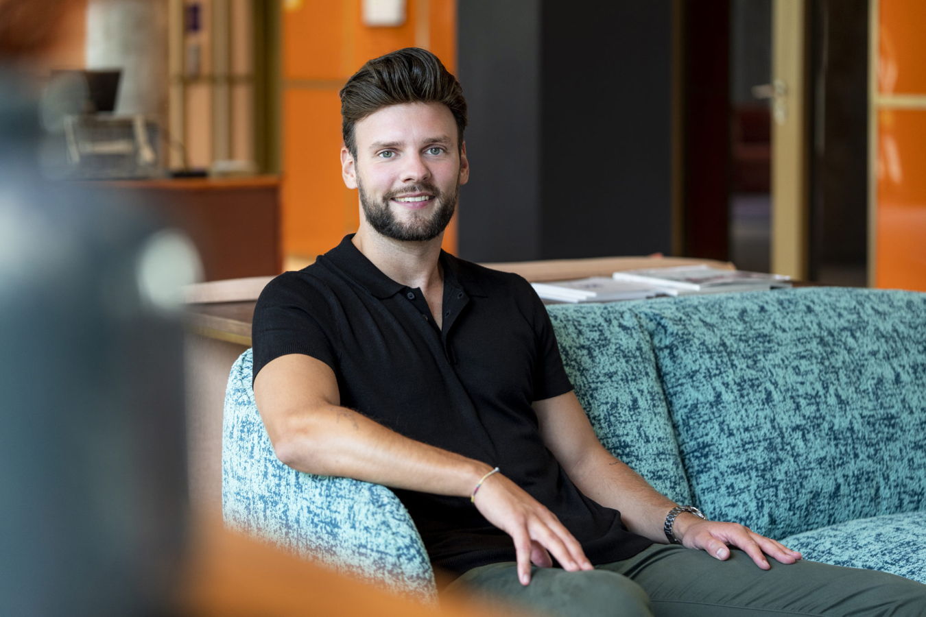 KMU und Mittelstand Ein lächelnder Mann sitzt auf einem türkisfarbenen Sofa in einem modernen Innenraum