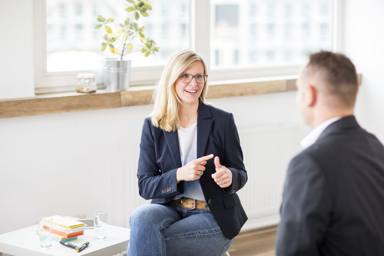 Zwei Personen im Gespräch in einem hellen Büro, die Frau gestikuliert und lächelt