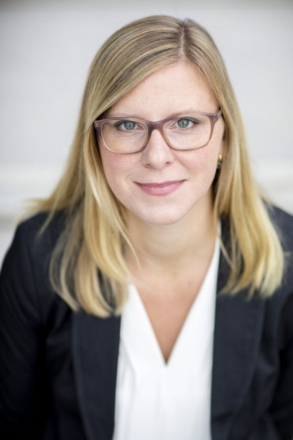Porträt einer Frau mit Brille und blondem Haar in schwarzem Blazer und weißer Bluse