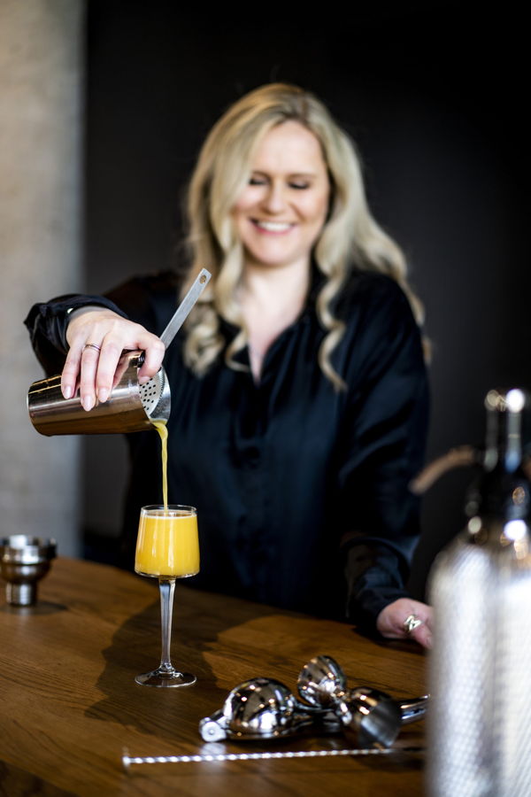Eine Frau gießt einen gelben Cocktail in ein Glas