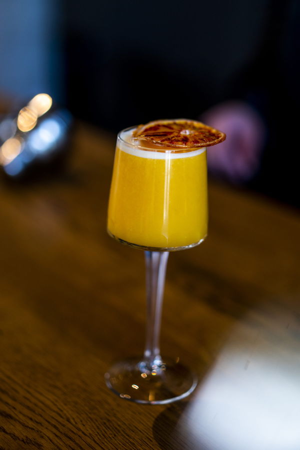 Gelber Cocktail in einem hohen Glas mit getrockneter Orangenscheibe