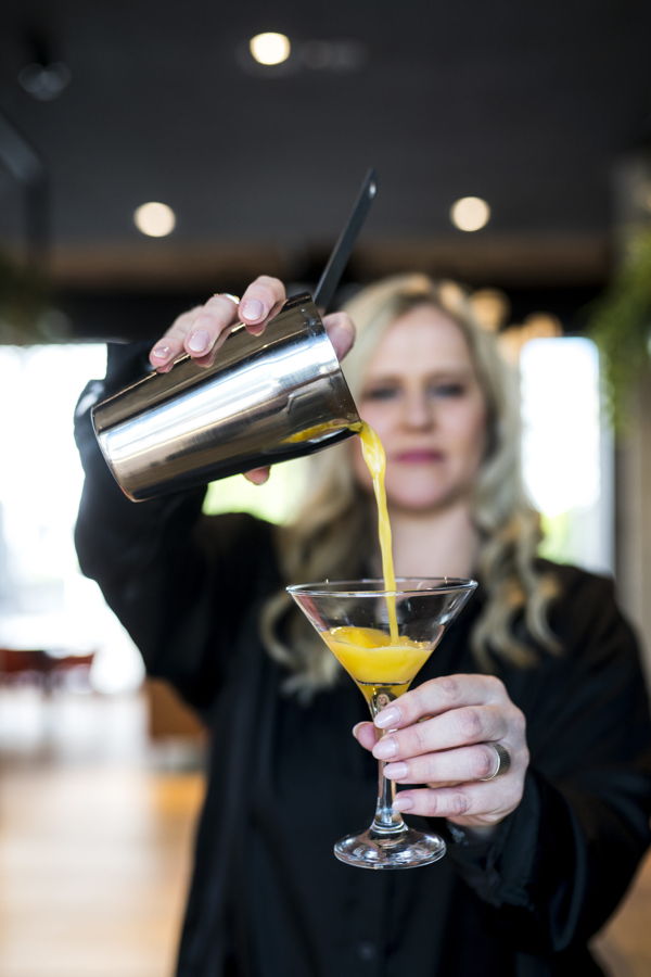 Eine Barkeeperin gießt einen gelben Cocktail in ein Martiniglas