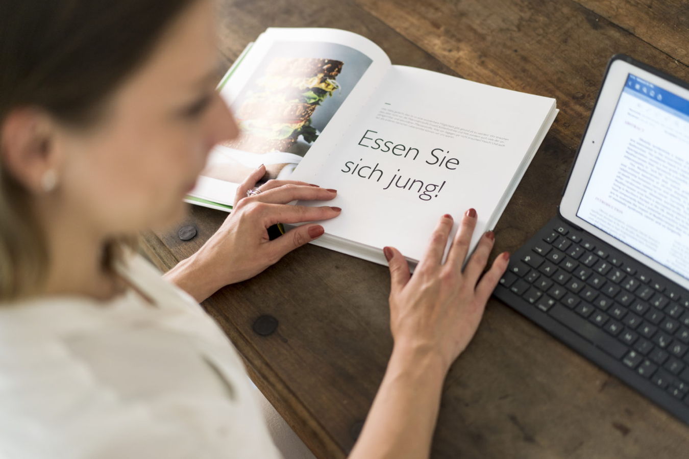 Frau liest ein Magazin mit der Aufschrift „Essen Sie sich jung!“ neben einem Tablet