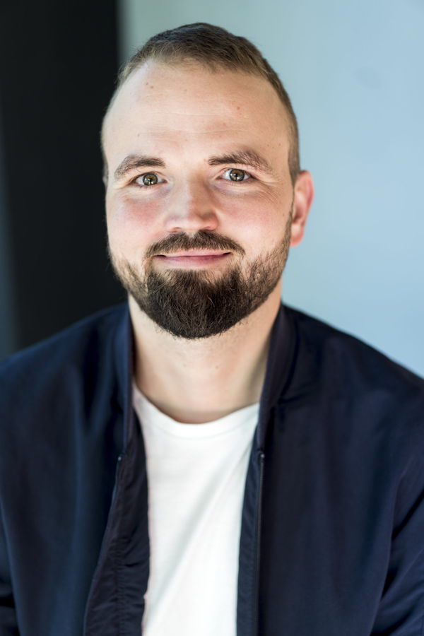 Porträt eines lächelnden Mannes mit Bart vor blauem Hintergrund