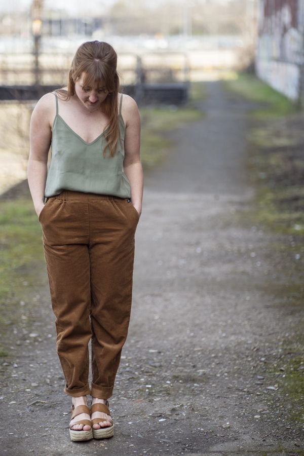 Eine Frau mit grünem Top und brauner Hose geht mit gesenktem Blick auf einem Weg