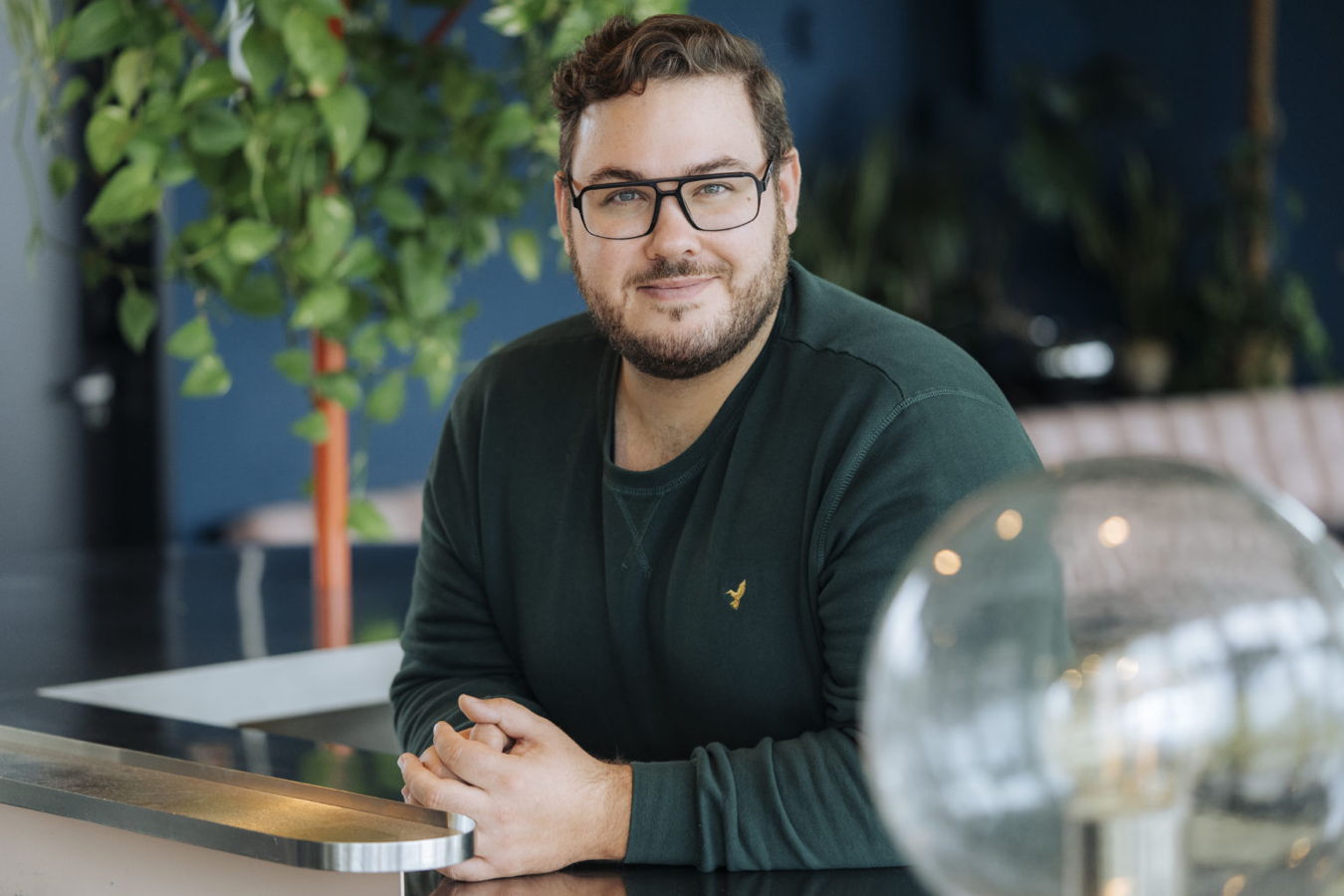 Mann mit Brille lehnt an einer Theke in einem modernen Innenraum