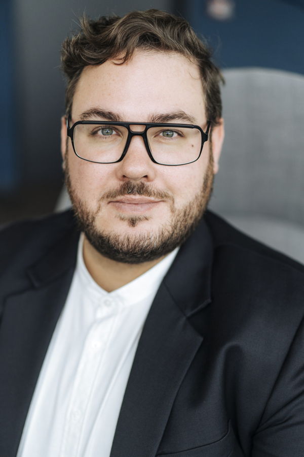 Porträt eines Mannes mit Brille im schwarzen Anzug und weißem Hemd