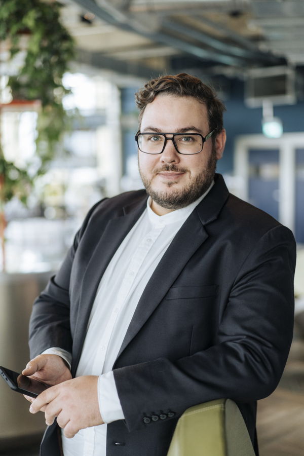 Mann im Anzug mit Brille hält ein Smartphone in einem modernen Büro