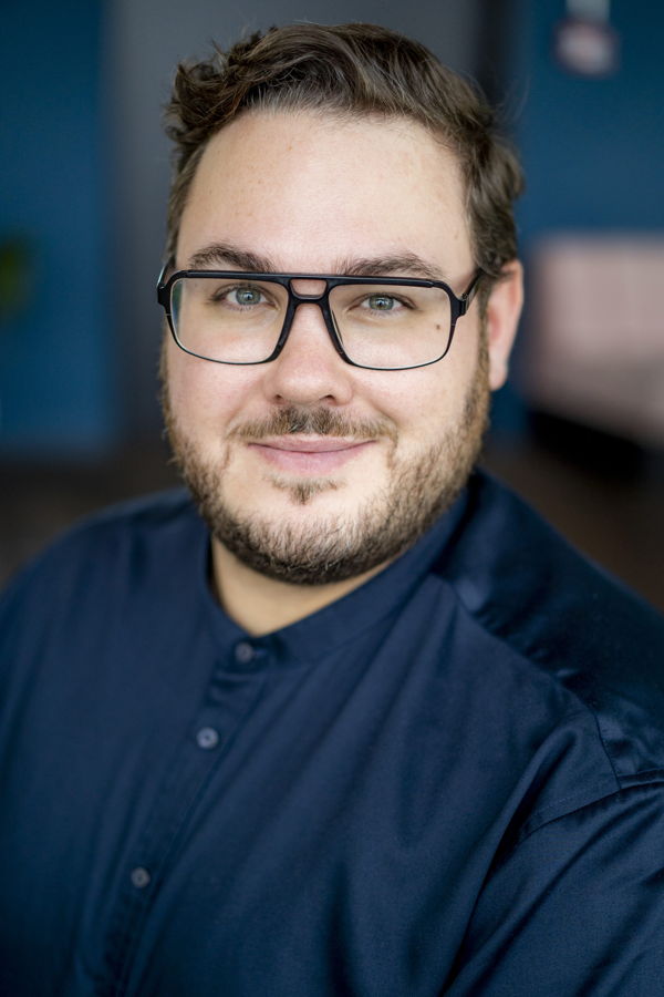 Porträt eines lächelnden Mannes mit Brille und dunklem Hemd
