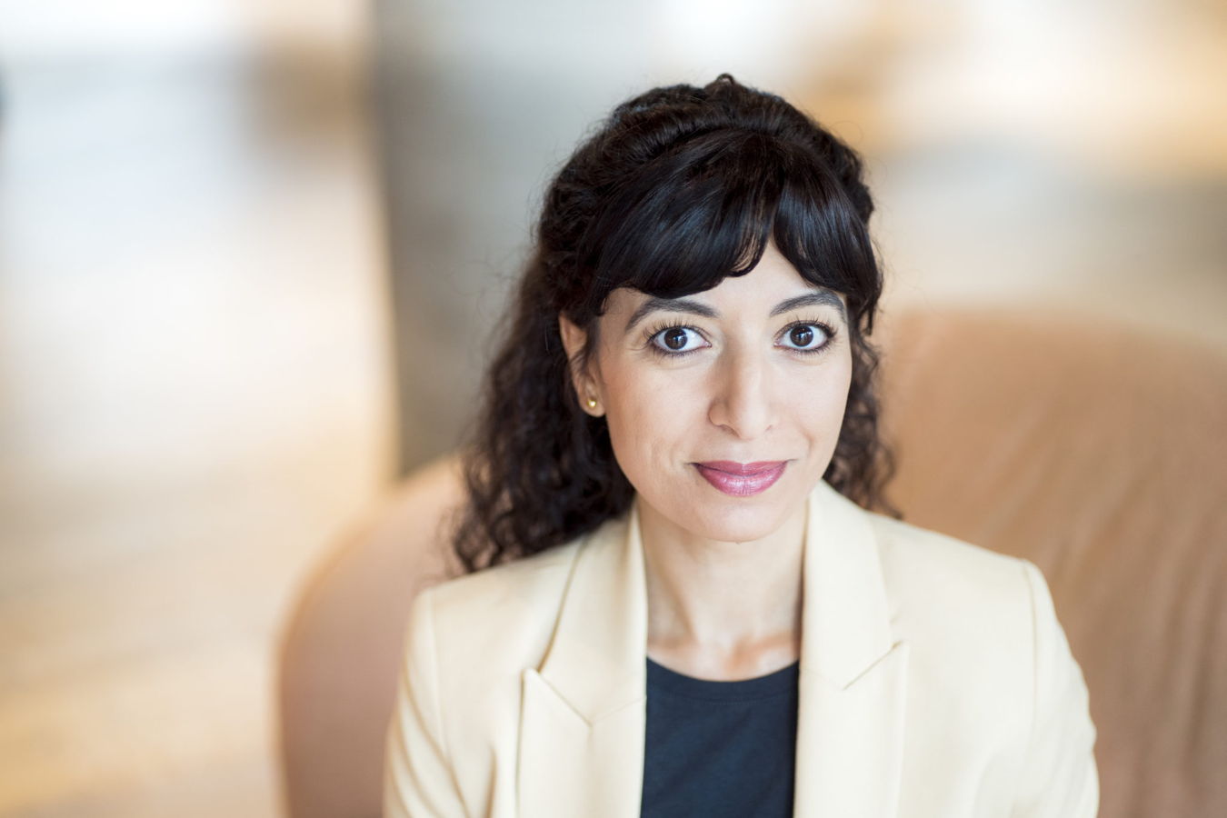 Porträt einer Frau mit dunklen Haaren und hellem Blazer vor unscharfem Hintergrund