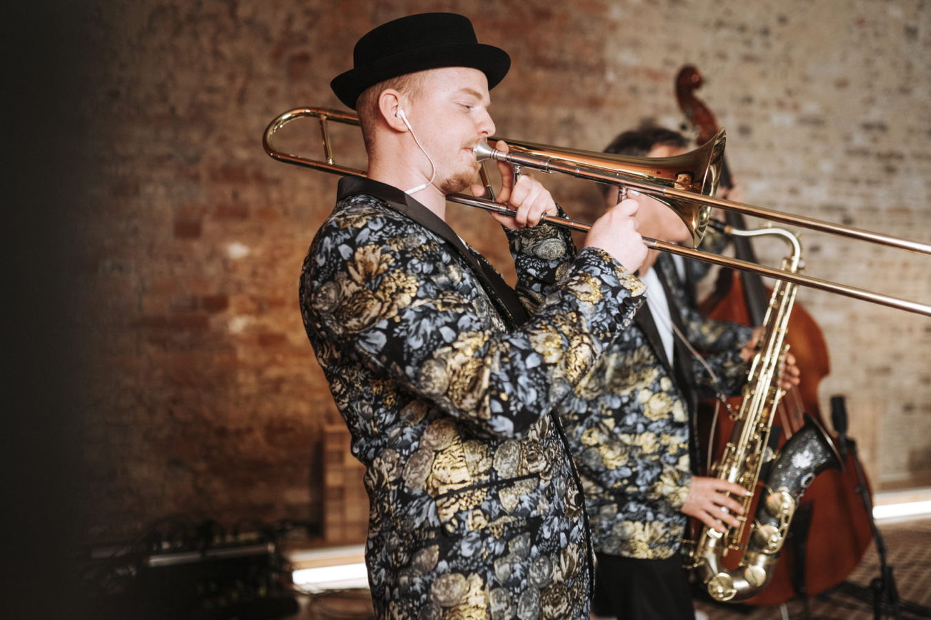 Ein Musiker im gemusterten Anzug spielt Posaune; im Hintergrund spielt ein Kontrabassist