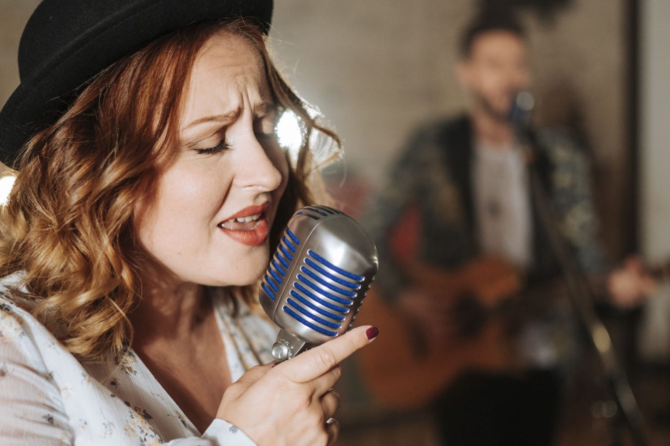 Frau singt in ein Retro-Mikrofon, im Hintergrund ein unscharfer Musiker