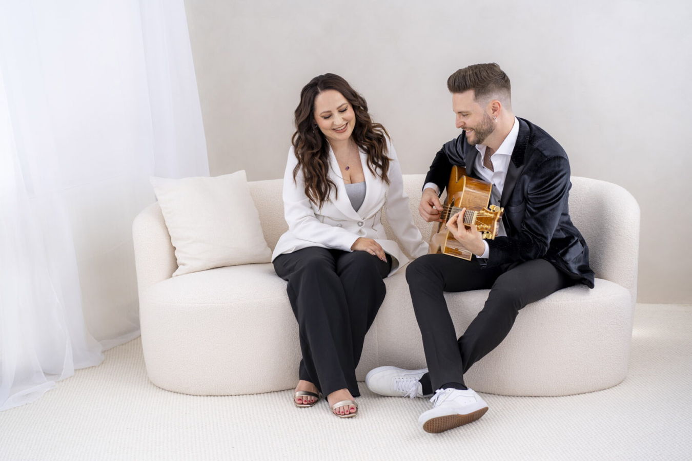 Ein Mann spielt Gitarre, während eine Frau lächelnd neben ihm auf einem Sofa sitzt