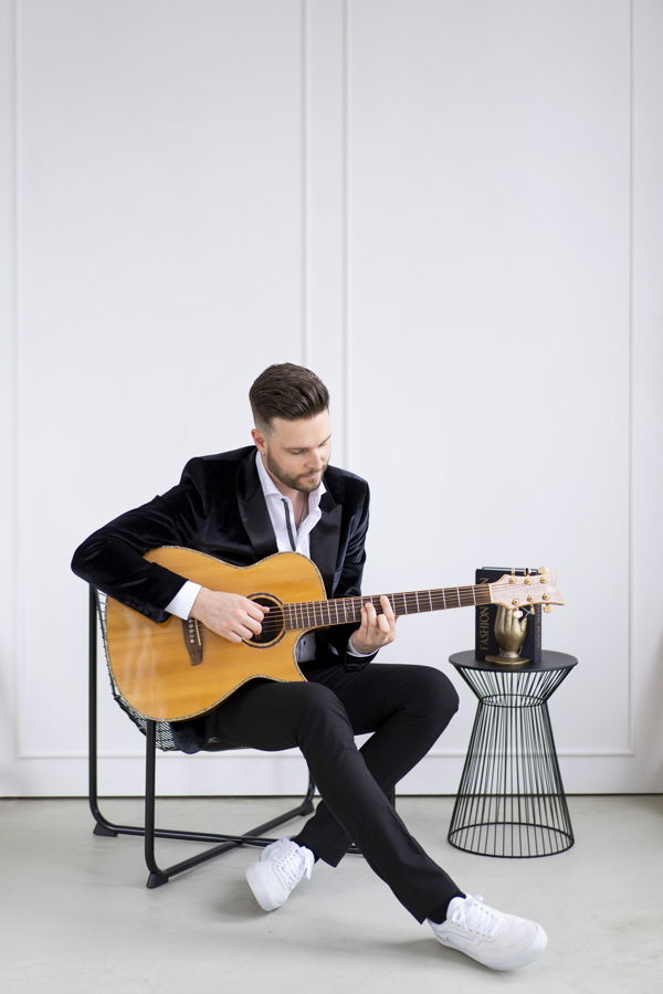 Mann im Anzug spielt Akustikgitarre auf einem Stuhl