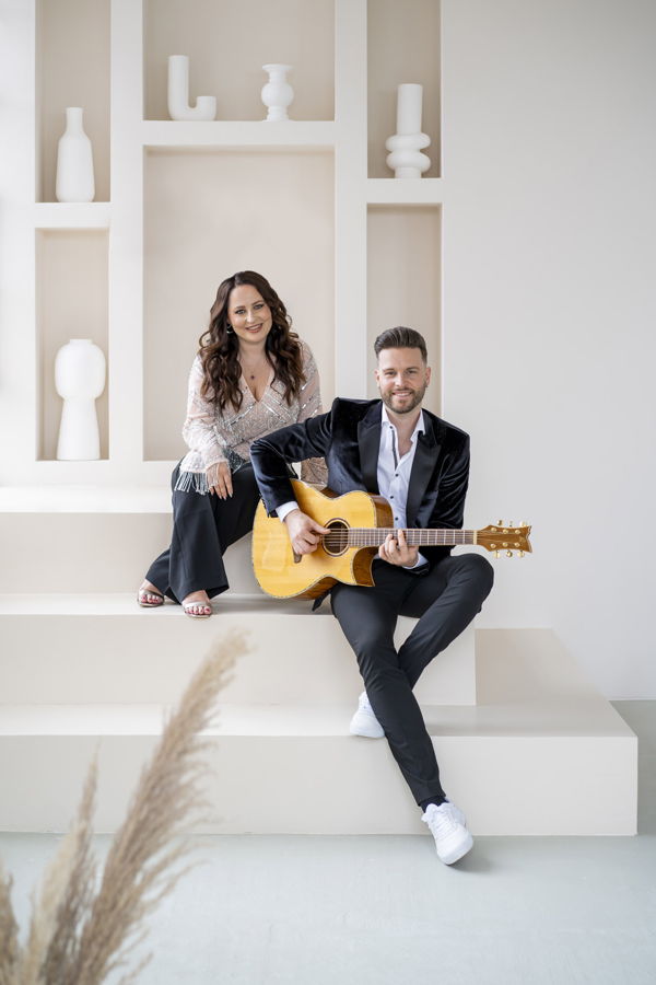 Ein Mann spielt Gitarre, während eine Frau neben ihm sitzt