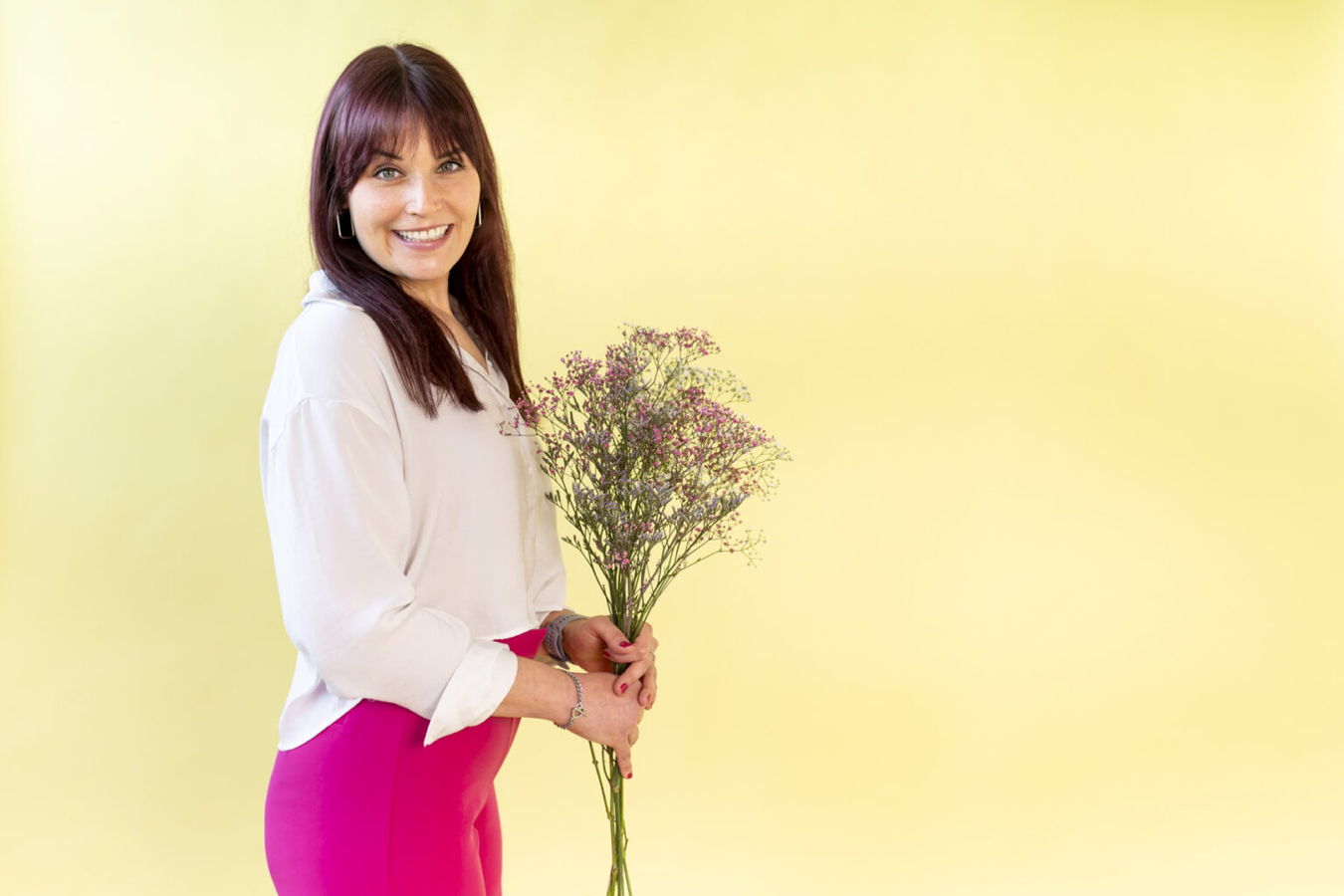 Lächelnde Frau mit langem dunklen Haar hält einen Blumenstrauß vor gelbem Hintergrund