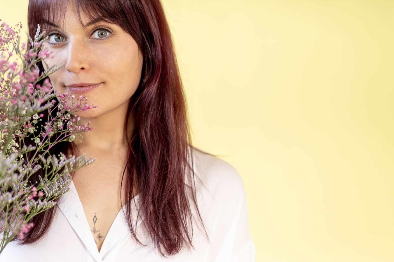 Porträt einer Frau mit roten Haaren vor gelbem Hintergrund, teilweise von pinken Blumen verdeckt