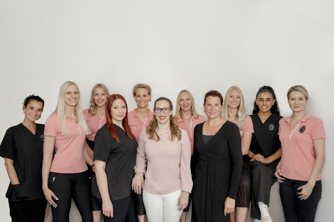 Gruppenfoto von zehn Frauen in rosa und schwarzen Arbeitskleidern vor hellem Hintergrund