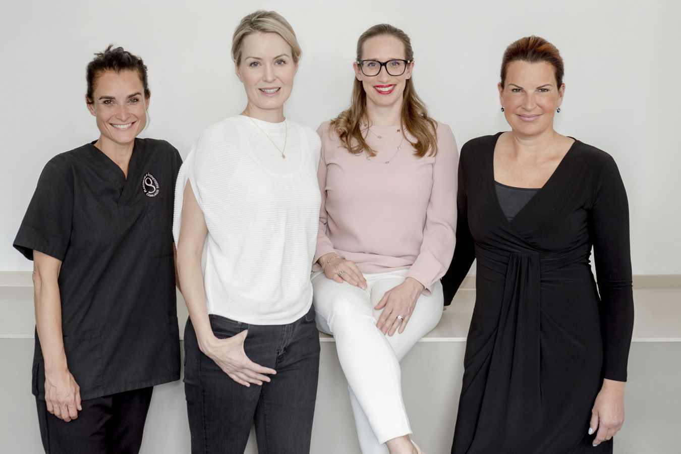 Vier Frauen stehen und sitzen vor einer hellen Wand