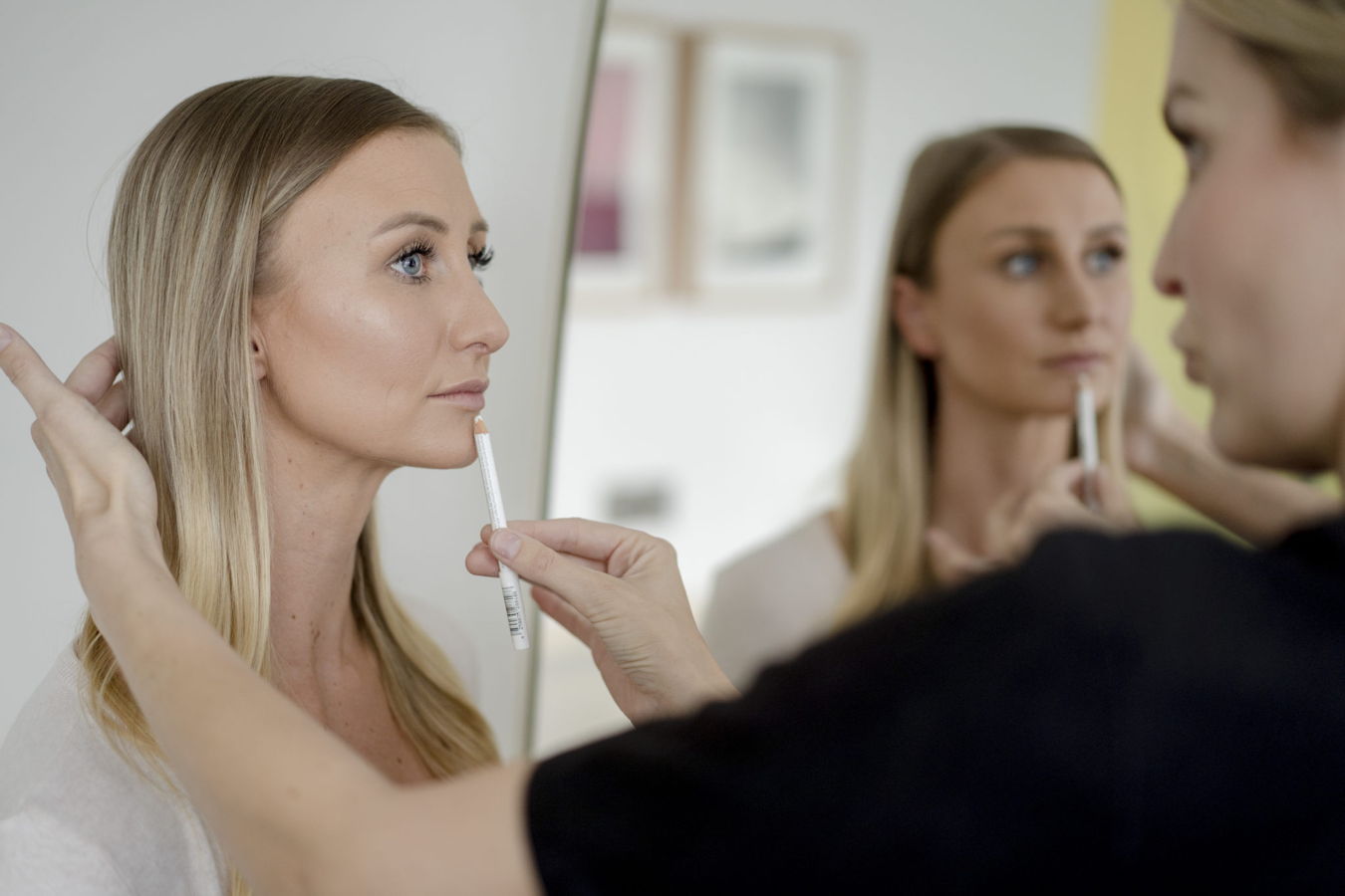 Eine Frau wird vor einem Spiegel mit einem Stift am Gesicht vermessen