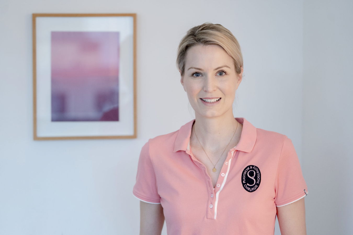 Porträt einer Frau in rosa Poloshirt mit Logo der plastisch-ästhetischen Chirurgie