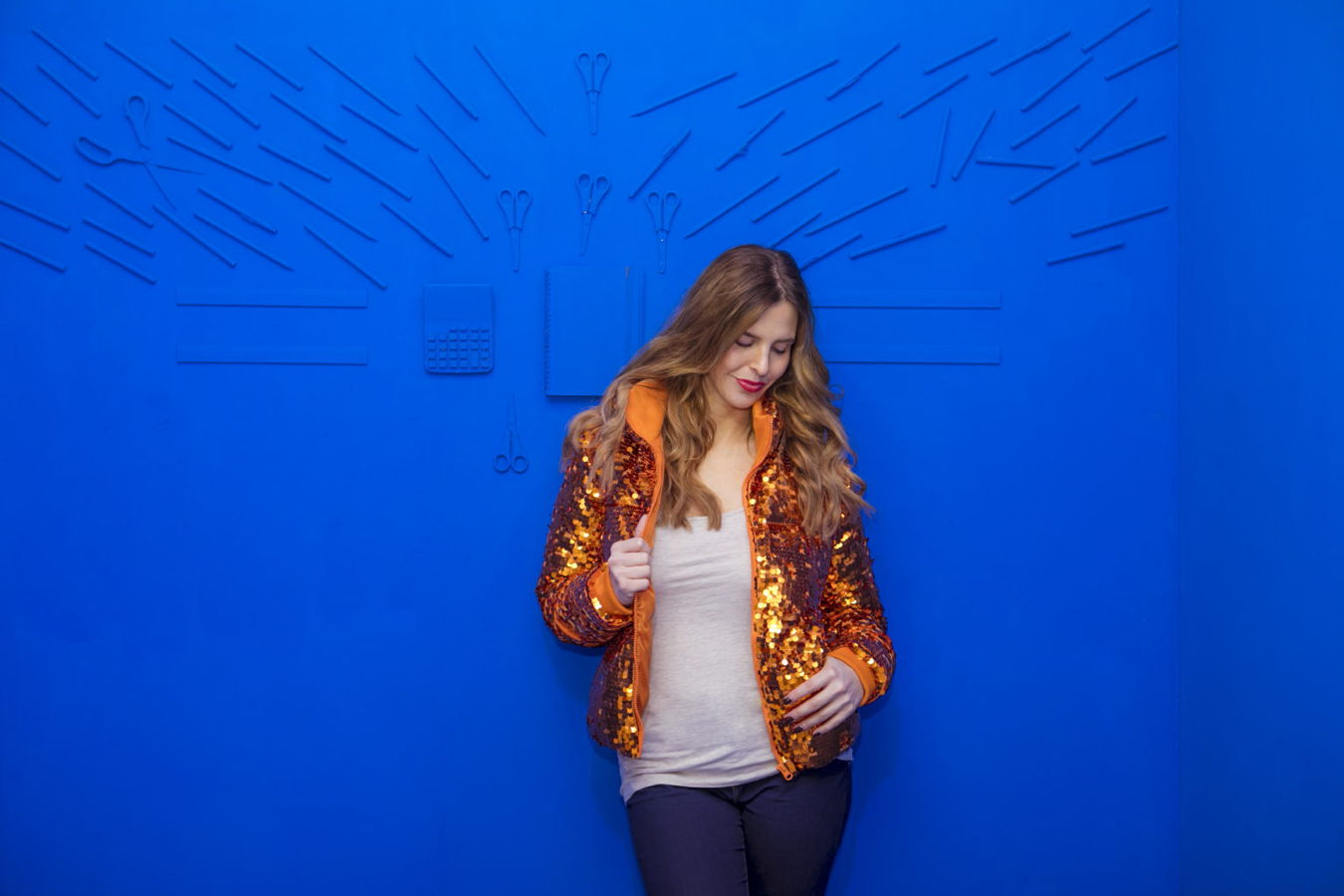 Frau in orangefarbener Paillettenjacke vor blauem Hintergrund