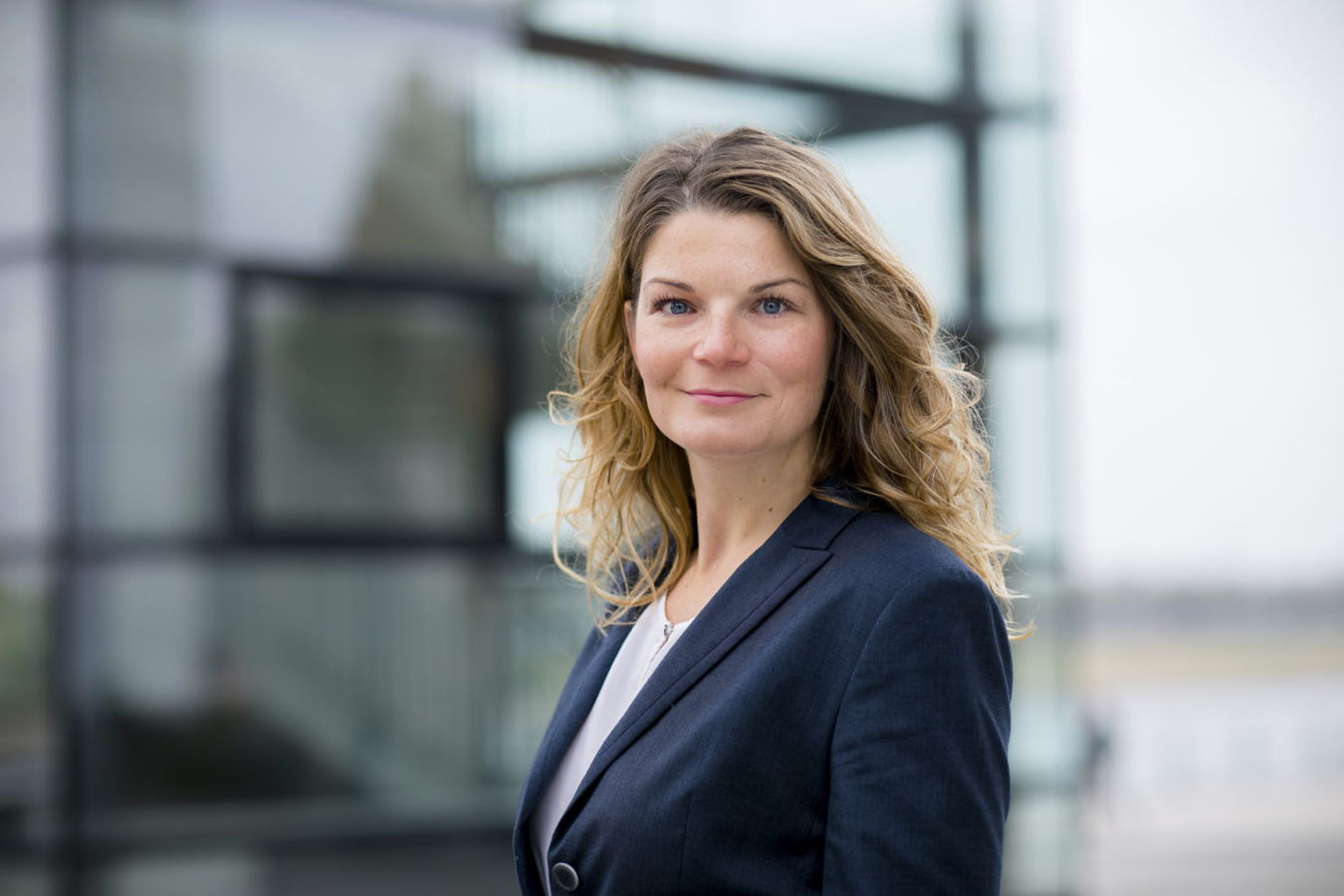 Porträt einer Frau im dunklen Blazer vor einem modernen Glasgebäude