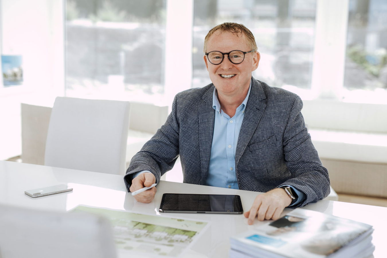 Mann in einem Büro sitzt an einem Tisch mit Tablet und Stift und lächelt in die Kamera