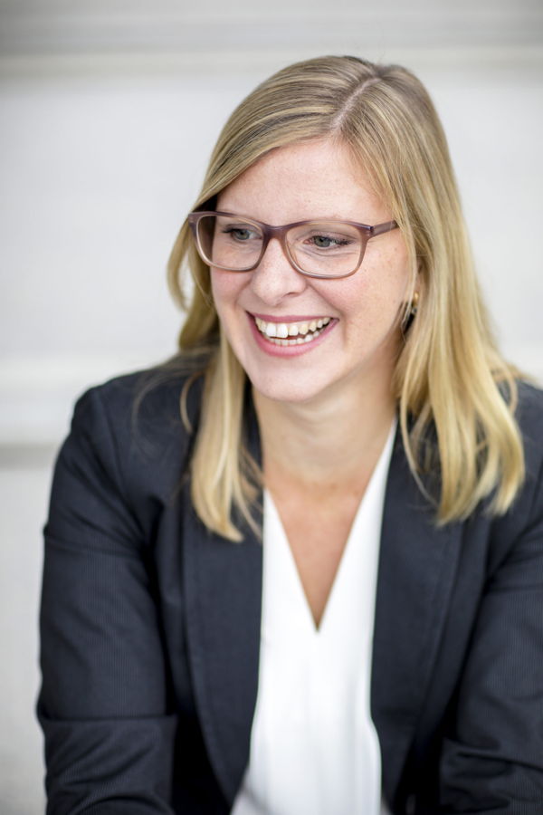 Lächelnde Frau mit Brille und blondem Haar im dunklen Blazer