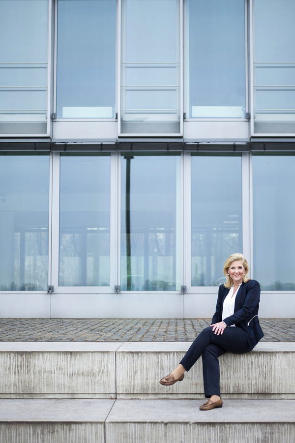 Frau im Anzug sitzt vor einem modernen Glasgebäude auf einer Steinbank
