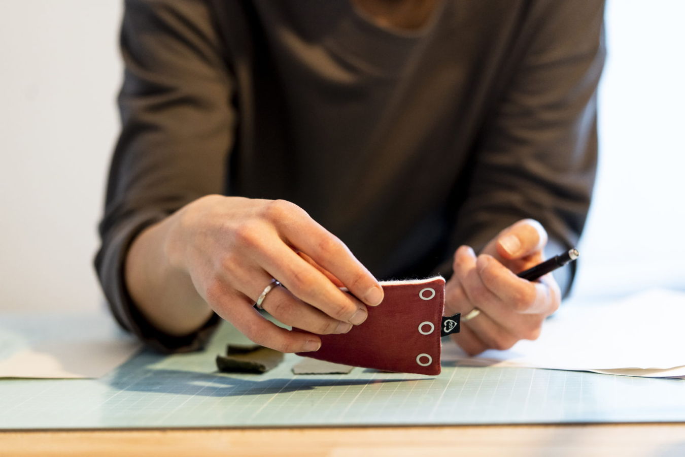 Person arbeitet an einem kleinen roten Stoffstück mit Stift auf einer Schneidematte
