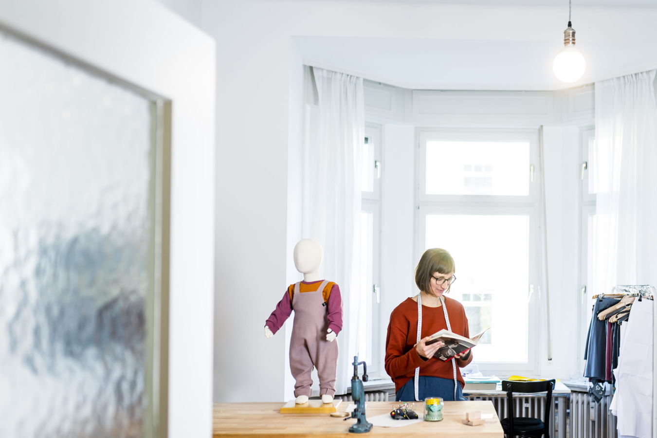Schneiderin liest ein Buch neben einer Kinderpuppe im Atelier