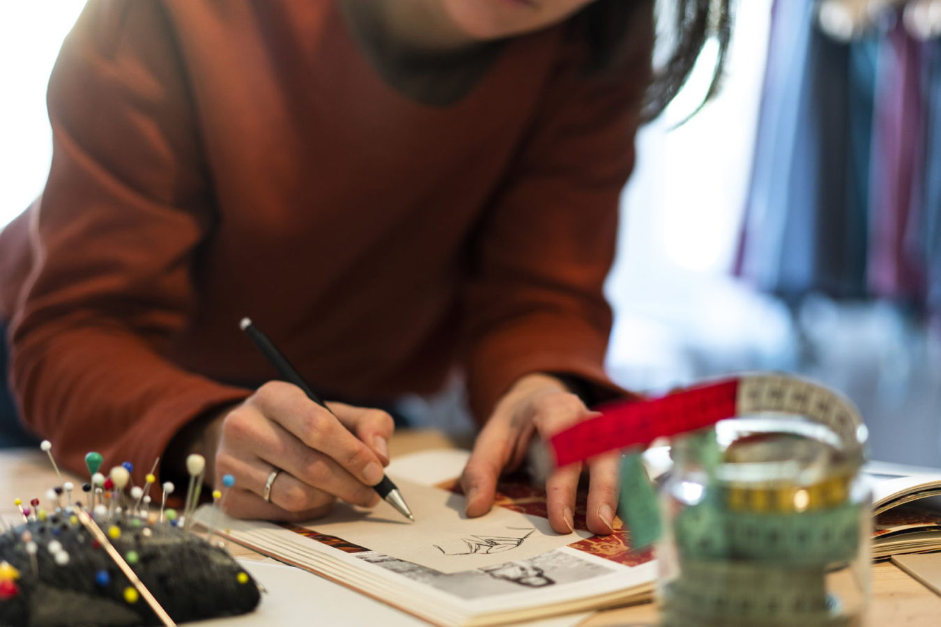 Person zeichnet mit einem Stift in einem Skizzenbuch am Tisch