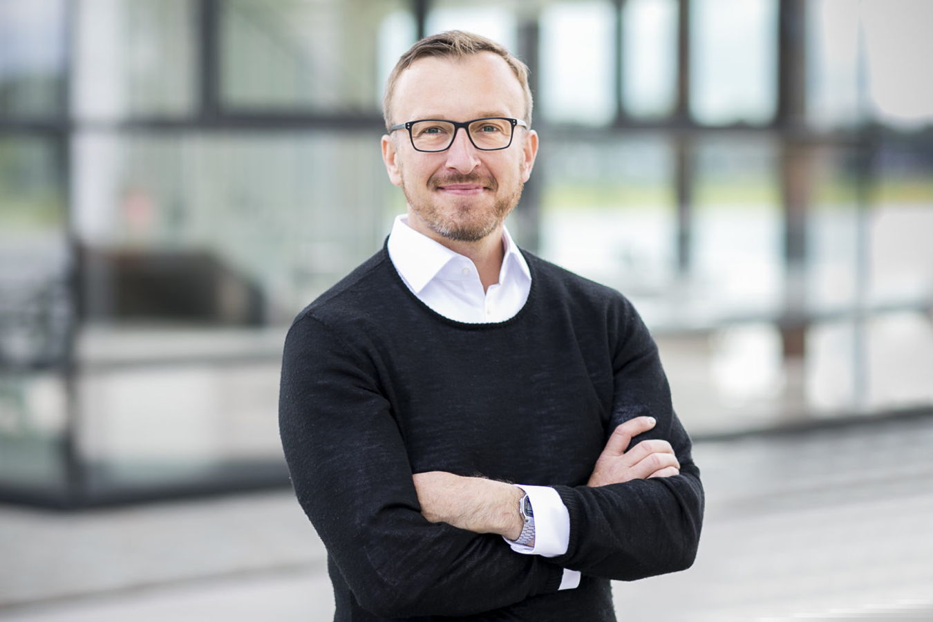 Trainer und Coach Porträt eines Mannes mit Brille und verschränkten Armen vor einem modernen Gebäude