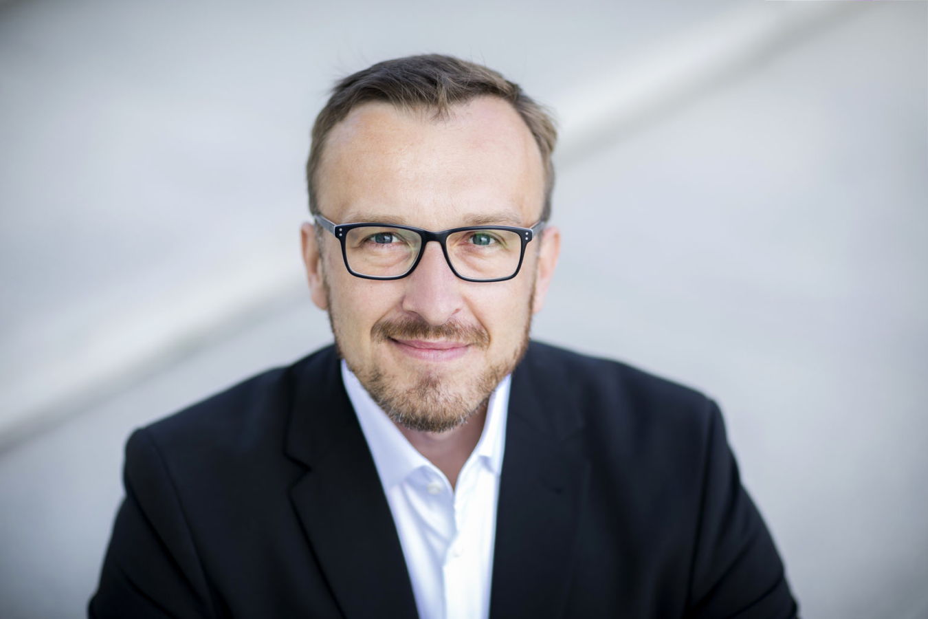 Porträt eines Mannes mit Brille im schwarzen Anzug und weißem Hemd
