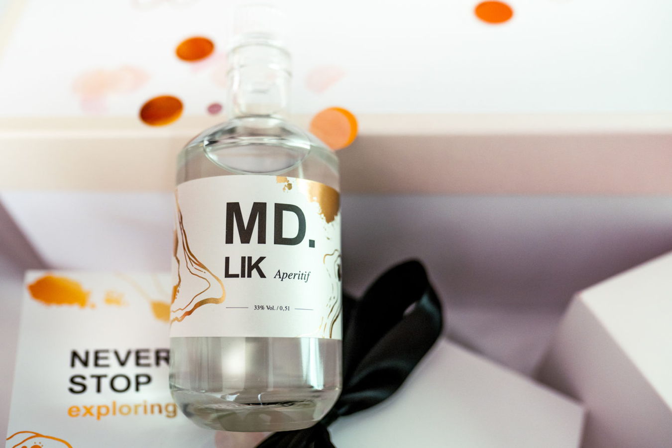 Flasche mit MD Lik Aperitif, 33 % Vol., vor einer Verpackung mit „NEVER STOP exploring“